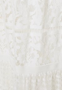 Biała koronkowa tkanina z kwiatowymi wzorami, geometrycznymi motywami oraz teksturowymi warstwami z gładkim białym paskiem. Składniki detaliczne w całym projekcie.