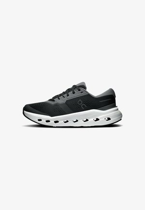 Chaussure de course athlétique noire et grise avec semelle blanche, dotée de plusieurs trous de ventilation latéraux et de lacets noirs.