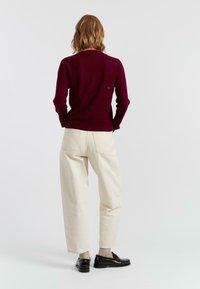Bordeaux sweater met een aansluitende pasvorm, gecombineerd met crèmekleurige broek met wijde pijpen. Zwarte instapschoenen maken de outfit compleet. Geverfd breisel.