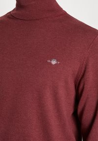 Bordeauxfarbenes Rollkragenpullover aus glattem Strickstoff. Mit kleinem GANT-Logo auf der Brust sowie geripptem Hals, Bündchen und Saum.