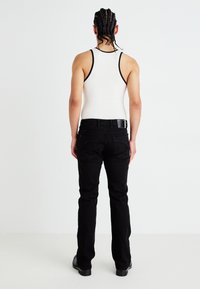 Svarta denimjeans med slim fit, med bakfickor och en svart lädermidjeaxel. Kombineras med en vit linne.
