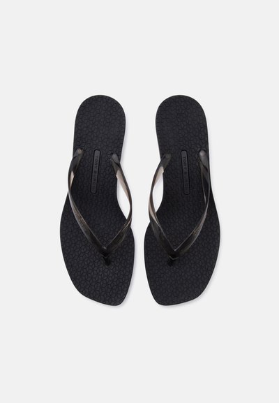Paire de tongs noires texturées avec des brides noires légèrement translucides placées côte à côte sur un fond blanc.