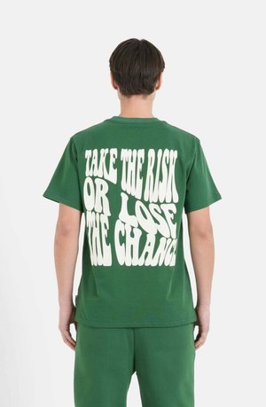 Grøn bomulds t-shirt med overdimensioneret hvid tekst på ryggen, der siger "TAG RISIKOEN ELLER TAB MULIGHEDEN", korte ærmer, afslappet pasform.