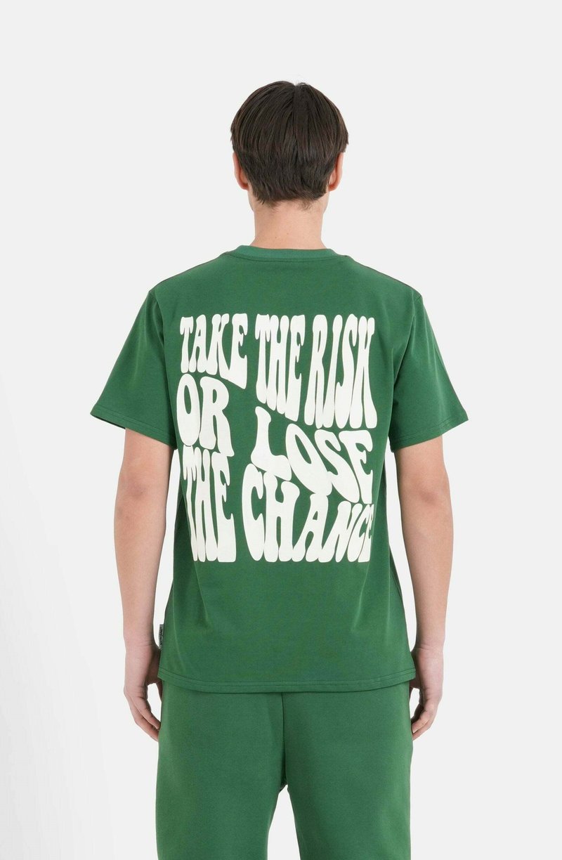 Camiseta de algodón verde con texto blanco de gran tamaño en la parte posterior que dice: "TOMA EL RIESGO O PIERDE LA OPORTUNIDAD", de mangas cortas y corte relajado.