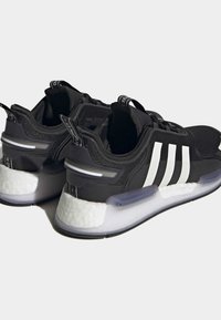 Svartvita atletiska sneakers med tre vita ränder, tjocka dämpade sulor och dragflikar på hälen och tungan.