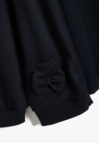Felpa blu navy con una texture morbida, polsini a costine e una tasca con un accento a fiocco. Il design è semplice e pratico.