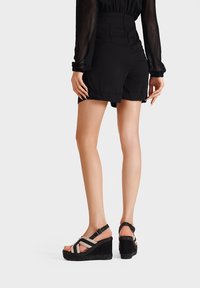 Sandali con zeppa e suola platform, realizzati in morbido suede nero e con dettagli in paglia beige, fissati con cinturini incrociati sulla parte superiore del piede.