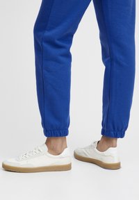 Hvide sneakers med gummisåler, tekstureret læderoverdel og snørebånd. Båret med blå tapered sweatpants med elastiske manchetter.