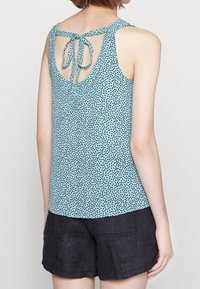 Top a maniche lunghe light blue con pois neri, design con schiena scoperta e dettaglio con fiocco, realizzato in tessuto morbido, abbinato a pantaloni corti scuri.