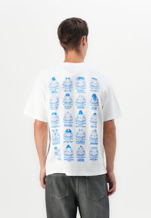 White cotton t-shirt featuring various blue graphic illustrations on the back, depicting cartoonish faces with musical genre labels beneath each one.