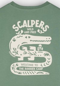 Vihreä pyöreäkauluksinen t-paita, jossa on valkoinen graafinen kuva käärmeestä, jota ympäröivät kasvi-aiheet sekä tekstit "SCALPERS WILD AND FREE" ja "WELCOME TO THE SUMMER CAMP."