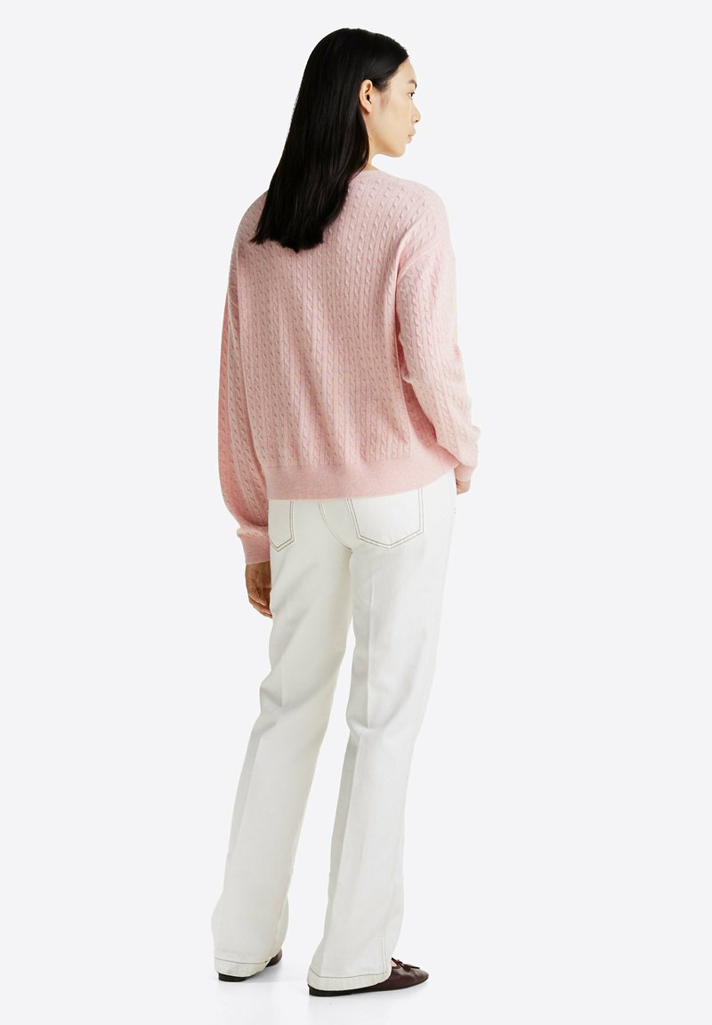 Lichtroze gebreide trui met een gestructureerd patroon, met een losse pasvorm en geribbelde manchetten, gecombineerd met witte wijde broekspijpen.