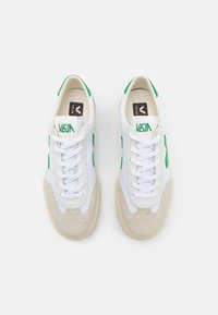 Baltas sneakers ar zaļiem akcentiem, ar gludu ādas virsu, zamša purngaliem un platiem baltajiem šņorēm. Logo atrodas uz mēles.