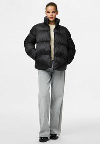 Chaqueta acolchada negra con alto cuello y diseño acolchado, hecha de un material suave. Combinada con pantalones vaqueros de pierna ancha en gris claro.