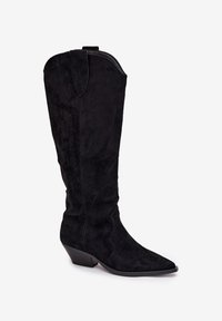 Botte noire en daim de style western, hauteur genou, avec bout pointu, bord supérieur incurvé et talon angulaire bas. Présente des détails de couture le long de la tige.