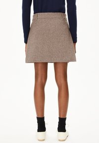 Personne portant une jupe mini en laine beige, un haut à manches longues bleu marine, des chaussettes noires et des chaussures à lacets blanches cassées, vue de dos.