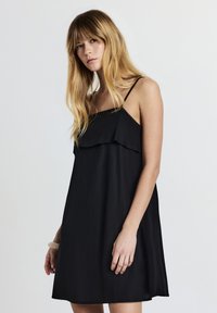 Abito nero senza maniche con un design a strati e volant sul petto, realizzato in un tessuto leggero, con spalline sottili e una vestibilità rilassata.