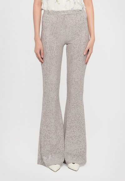 Flared trousers in light gray fabric with small shiny accents. Features a stretchy waistband and straight fit, ending above pointed white shoes.