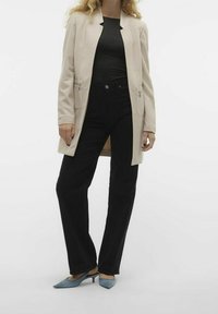 Beige dlouhý blazer s texturovaným povrchem, přiléhavý černý top, černé široké kalhoty a modré lodičky s špičatou špičkou. Hladká látka a minimalistický design.