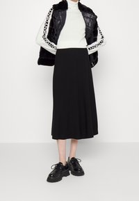 Svart midiklänning med utsvängd design, bärs med en vit polotröja och en svart faux fur-puffjacka. Svarta klumpiga skor.