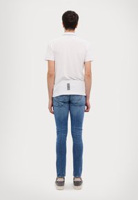 White polo with short sleeves, featuring a black stripe on the collar and a vertical black pattern at the back, paired with blue jeans.