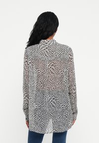 Sheer black and white patterned shirt with a collar, long sleeves, and a curved hem. Lightweight fabric features a swirling design.