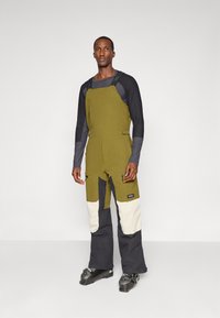 Mala de esqui verde oliva e preta com alças ajustáveis, bolsos laterais, painéis brancos contrastantes nas pernas e um corte largo.