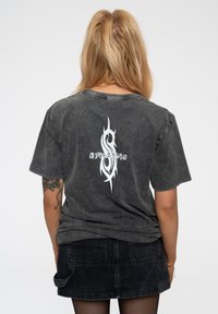 Black, oversized t-shirt featuring a white flame-like graphic and text on the back. Made of soft, worn fabric with a relaxed fit.