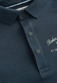 Polo de color azul marino con collar acanalado, tres botones negros en la tapeta y logo bordado en blanco en el pecho.