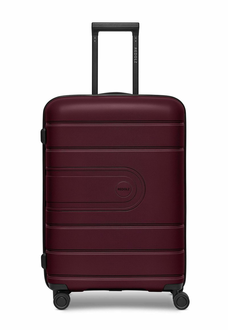Valigia rossa in bordeaux, realizzata in plastica rigida testurizzata, dotata di manico telescopico e quattro ruote nere per la mobilità.