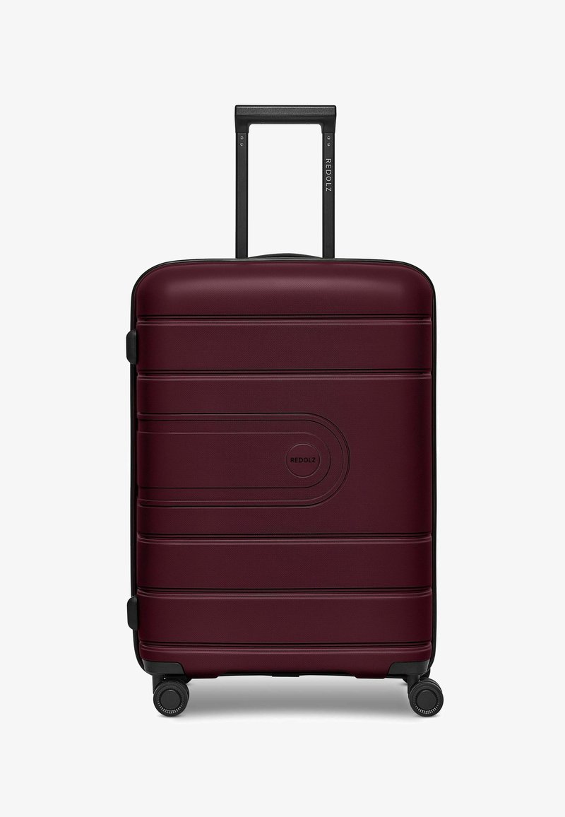 Valigia rossa in bordeaux, realizzata in plastica rigida testurizzata, dotata di manico telescopico e quattro ruote nere per la mobilità.