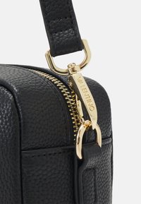 Černá kožená taška s texturovaným povrchem, zlatým zipem a kovovými doplňky. Vybavená odnímatelným popruhem a vyraženým logem.