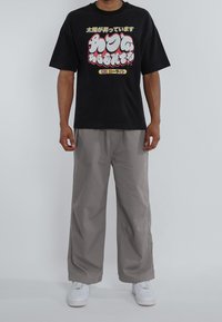 Black short-sleeve T-shirt with colorful Japanese text design, paired with light gray loose-fitting pants and white sneakers.