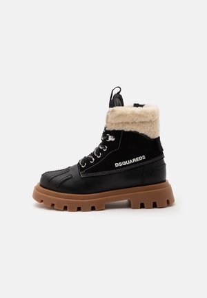 Bottine noire DSQUARED2 à la cheville avec semelle épaisse à crampons marron, lacets à l'avant, coutures blanches et col en shearling beige sur fond blanc.