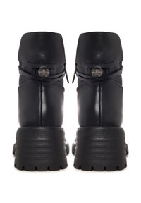 Botas ankle de piel negra con punta redondeada, cierre de cremallera y suela gruesa texturizada. Un detalle notable incluye una correa decorativa con un emblema de metal.