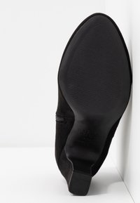 Černé semišové boty na podpatku s špičatou špičkou a zipovým detailem po straně. Podešev je z texturované gumy, která zajišťuje přilnavost a trvanlivost.