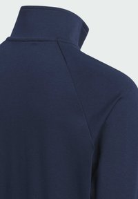 Haut bleu marine à col montant avec une texture lisse. Dispose de manches raglan et d'un design épuré et minimal sans fermetures visibles.