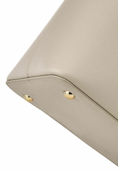 Bežni vogal teksturirane usnjene torbe z vidnim šivanjem in dvema okroglema zlatima kovinskima zakovicama na spodnjem robu.