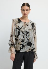 Blusa nera e beige con motivo floreale, scollo arricciato, maniche lunghe con polsini svasati e dettaglio a fiocco sul davanti. Tessuto leggero.