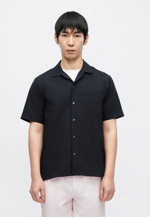 Short-sleeve black shirt with a textured fabric, featuring a button-up design and a chest pocket. Paired with light pink shorts.