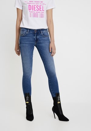 Niebieskie dżinsy o dopasowanym kroju, zestawione z czarnymi szpiczastymi botkami na wysokim obcasie oraz białym T-shirtem z różowym napisem.