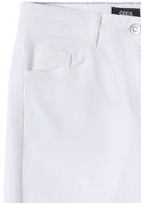 Vaqueros blancos de mezclilla en primer plano que muestran el bolsillo delantero, pequeño bolsillo para monedas, presilla para el cinturón, cintura y botón plateado con etiqueta de marca dentro de la cintura.
