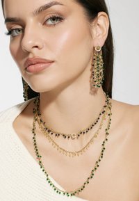 Gouden sieradenset met gelaagde kettingen en hangende accenten. Bevat smaragdgroene en marineblauwe kralen, gecombineerd met glinsterende details.