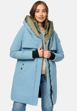 Light blue puffer coat with a detachable olive green hood, front zipper, snap buttons, and ribbed black cuffs, shown over a beige sweater.