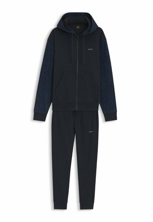 Sweat à capuche zippé bleu marine avec manches texturées et pantalon de jogging assorti, tous deux ornés de petits logos « BOSS » sur la poitrine et la cuisse.