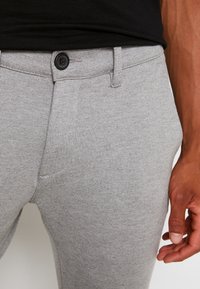 Grijze, passend zittende broek gemaakt van een zachte, gestructureerde stof met een knoopsluiting en zijzakken. Eenvoudig ontwerp met een gladde afwerking.