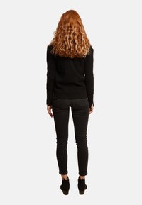 Czarny sweter z długimi rękawami, noszony z obcisłymi czarnymi jeansami i botkami, widziany od tyłu. Kręcone włosy opadające za ramiona.