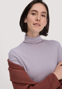 Hellblau-lila Rollkragenoberteil mit taillierter Form, kombiniert mit einem strukturierten, rostfarbigen Strickmantel, der weiche Materialien und glatte Texturen präsentiert.