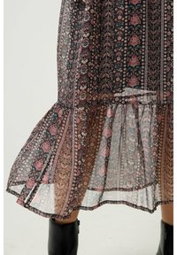 Vestido negro con estampado floral y dobladillo en capas, que presenta patrones multicolores de hojas y flores. La tela semitranslúcida añade textura.