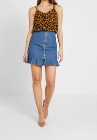Top in stampa leopardata con spalline sottili abbinato a una minigonna di denim con zip frontale e orlo a balze.